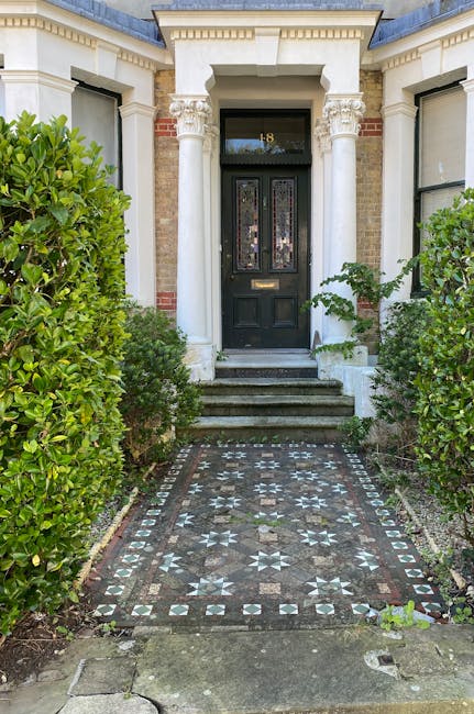 The image depicts the front entrance of a traditional terraced house with a black front door set within a white brick and stucco façade. The door features decorative stained glass panels and a letter